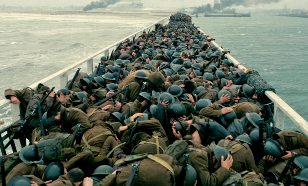 Crowded pier with soldiers in helmets crouching closely together during the Dunkirk evacuation in Dunkirk (2017).