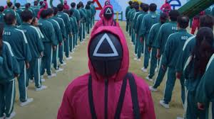 quid Game guard in a pink uniform with a triangle mask overseeing players in green tracksuits